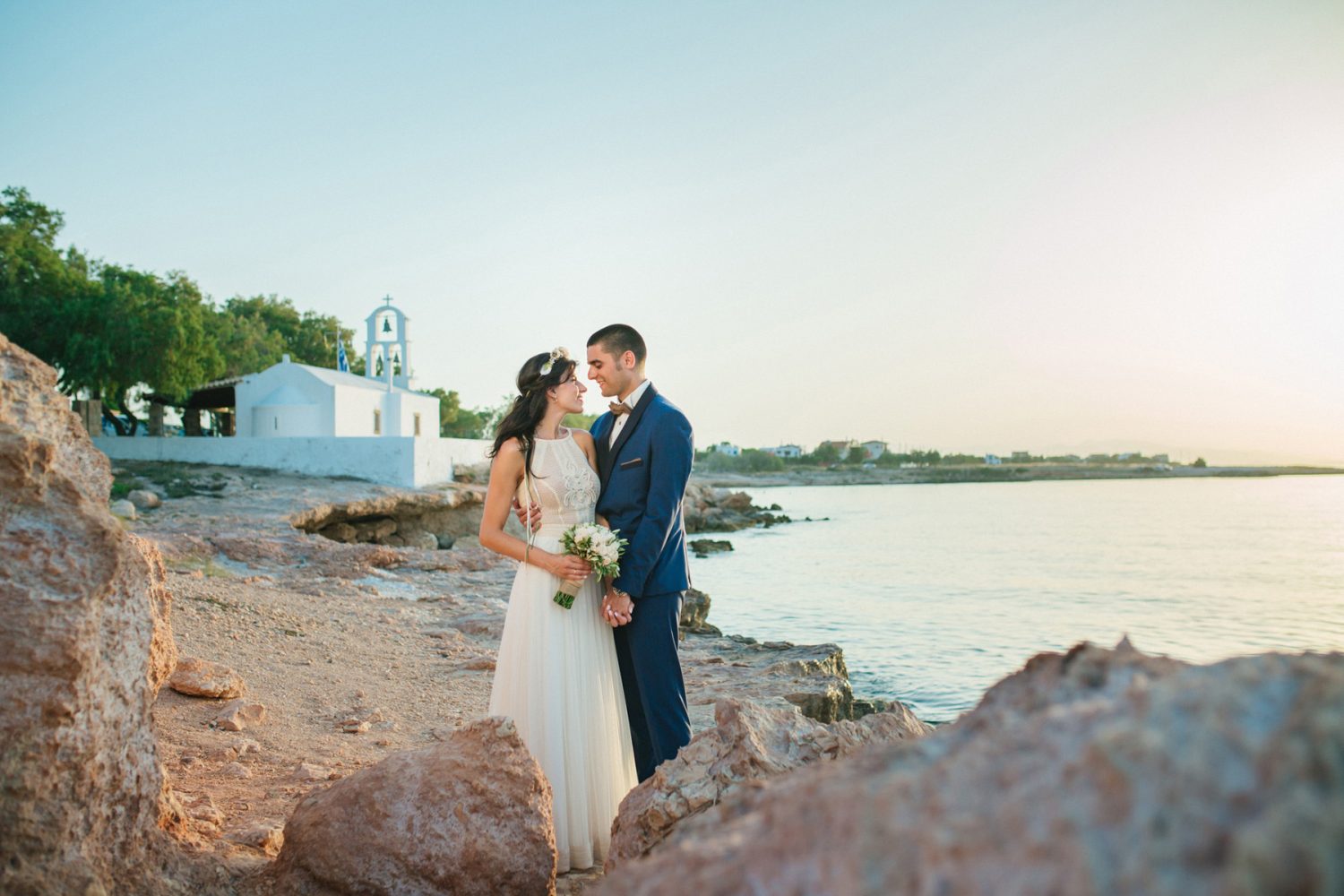 Couple posing in front of a seashore chapel, a their wedding in Aegina island
