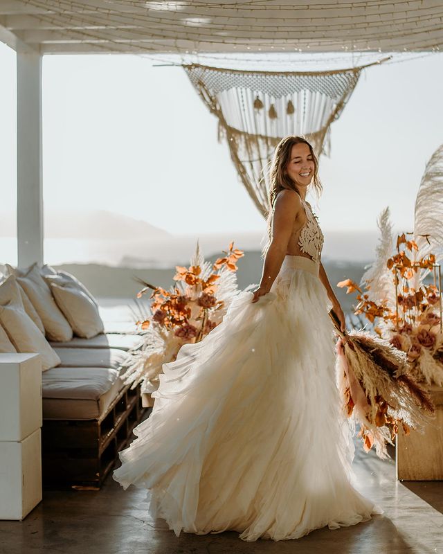 Bride in a handmade bridal dress with a crochet top by Atelier Zolotas, during her island destination wedding, framed by orange wild flowers and macrame wedding decoration