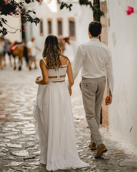 Back of a bride in boho-vintage, ethereal wedding dress by Atelier Zolotas, holding the hand of her partner, during their destination wedding in Hydra island